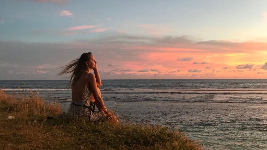 A woman sat on a clif fand looking out to sea,