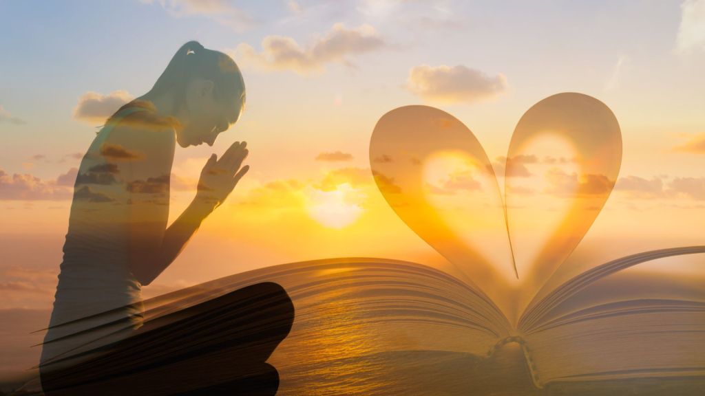  woman praying at sunrise. The pages of a bible form a heart shape overlaid onto the image